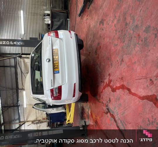 רכב לבן במוסך על רצפת בטון אדומה